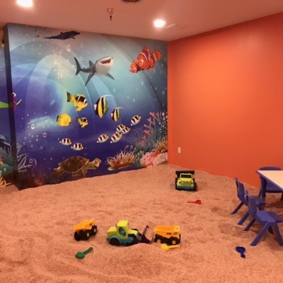 Children's salt room with toys on a salt covered floor in a red room with a decorative wall that has 'Finding Nemo' wallpaper