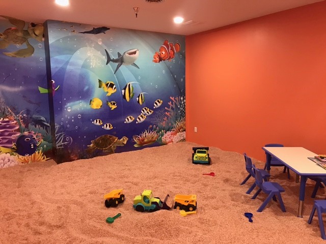Children's salt room with toys on a salt covered floor in a red room with a decorative wall that has 'Finding Nemo' wallpaper