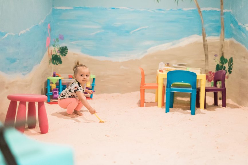 Halotherapy room with a young girl on a salt-covered floor with a play table and toys at the Serenity Salt Spa LLC in Forest Hill, Maryland