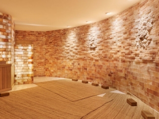 Sojo Spa Club. Rounded Spa Room With Salt Bricks On The Walls. Floor Is Covered By Tan Rugs.