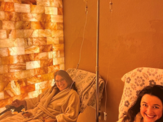 Sweet Be Wellness And Skin Clinic. Two Women In White Robes Sitting In Reclined Chairs While Hooked Up To Iv Next To Salt Tiled Wall