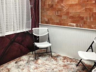Taste Of Health. White Foldable Chairs In Small Salt Room On Top Of Salt Covered Floor. The Salt On The Floor Is A Mixture Of White, Brown And Black Salt.