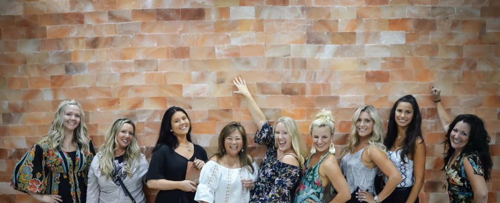 The Salt Center. 9 Women Up Against Salt Tiled Wall Posing For A Picture Together.