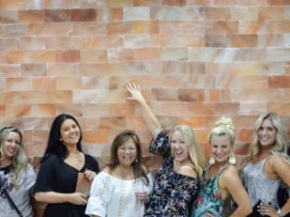The Salt Center. 9 Women Up Against Salt Tiled Wall Posing For A Picture Together.