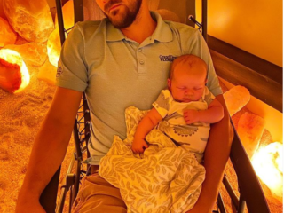 Eating Elevated. Man sitting in reclined chain with baby in his lap while in a lit salt room