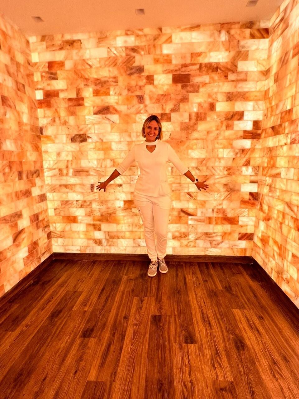 Dr. Rosaly Pichardo Standing In A Salt Room In Front Of A Himalayan Salt Brick Wall.