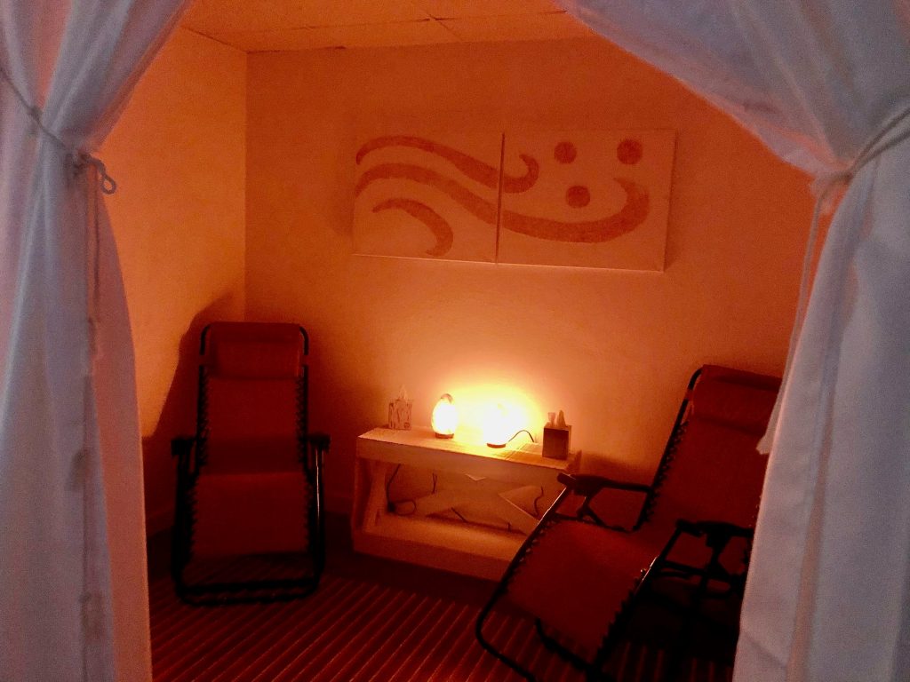 Massage by Andrea Yeager. A small, cozy room with two red lounge chairs in it. Between them is a lit candle. The opening of the room has an adjustable curtain for privacy.