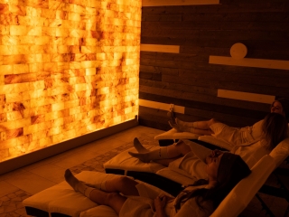 Three Women Relaxing On White Chaises In Front Of An Orange Backlit Salt Wall At The Sharper The Medical Spa In Fishers, Indiana