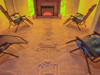 Radiant Well-Being. Four Lounge Chairs In Salt Room Facing A Fireplace. Above The Fireplace Are 5 Salt Rocks Which Are Glowing. Through The Middle Of The Room, The Word &Quot;Breathe&Quot; Is Written In The Salt.