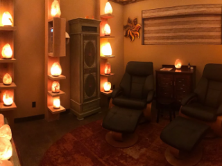 The Mandarin Spa At New Leaf. Dimly Lit Spa Room Has Two Chairs In It With Numerous, Glowing Salt Rocks On Shelves All Around The Room.