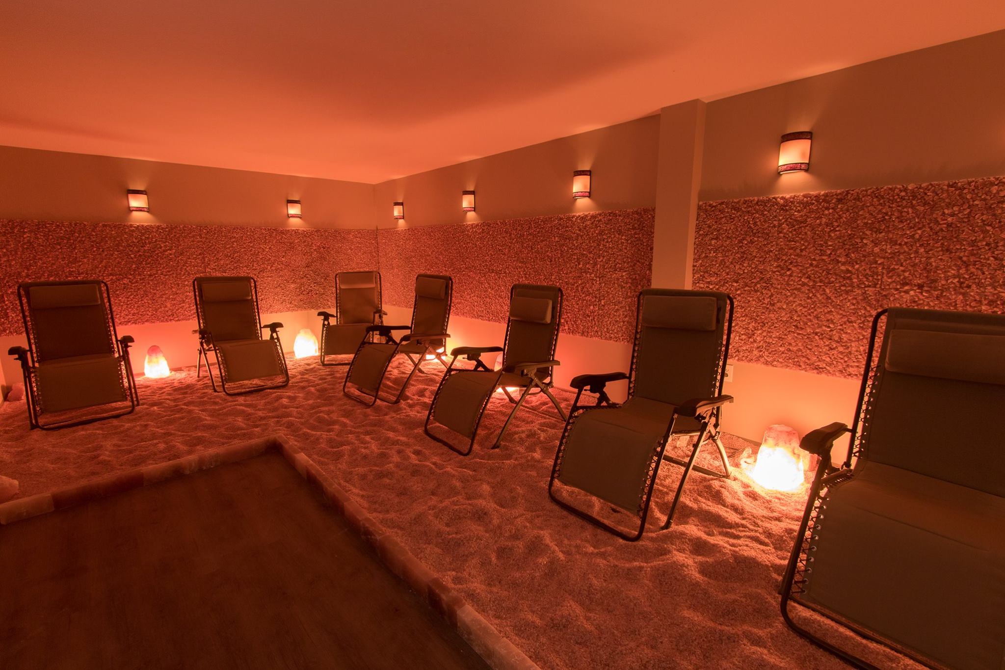 Seven Reclining Chairs In A Dimmed Room On A Salt-Covered Floor With A Centering Line Of Pink Salt Panels Around The Room At The Be Still And Breathe Salt Wellness Center - Lebanon, Tennessee.