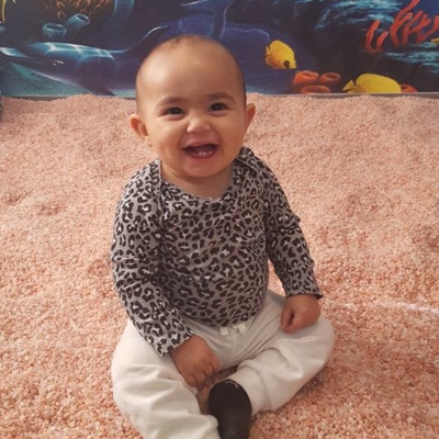 Baby smiling sitting on a salt-covered floor with an ocean wallpaper at the Be Still & Breathe Salt Wellness Center in Lebanon, TN