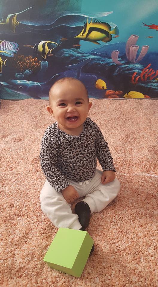 Baby smiling sitting on a salt-covered floor with an ocean wallpaper at the Be Still & Breathe Salt Wellness Center in Lebanon, TN