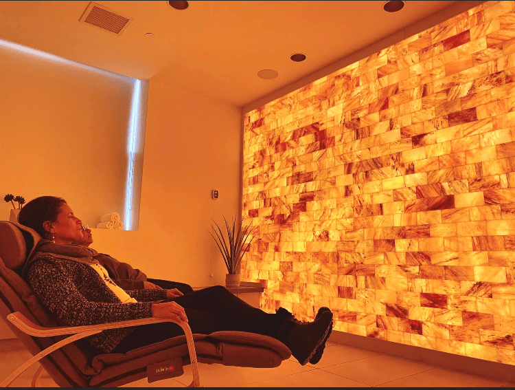 Two People Relaxing In Lounge Chairs In Front Of A Large Salt Brick Wall, Backlit By Led Lights At Beth Abraham Center For Rehabilitation And Nursing In Bronx, New York
