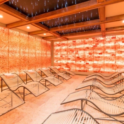 Ten White And Black Chaises With White Headrests On A Salt-Covered Floor Surrounded By Two Himalayan Salt Stone Walls And A Backlit Paneled Salt Stone Wall With Orange Lighting.