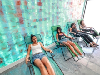 4 Women Relaxing In Lounge Chairs In Front Of A Green Colored Salt Brick Wall At Boca Cryo In Boca Raton, Florida