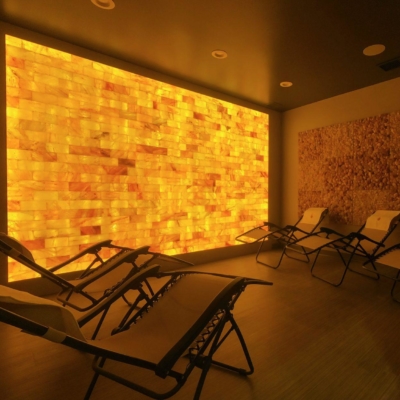 Five Reclining Chairs On A Brown Vinyl Floor With An Orange Backlit Salt Stone Wall And Two Large Rectangular Himalayan Salt Stone Décor On The Long Walls.