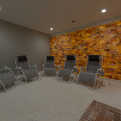 Five Reclining Chairs In A Grey Room On A White Slat-Covered Floor With Himalayan Salt Panels At The Breathe Salt And Sauna - Johnson Creek, Wisconsin.