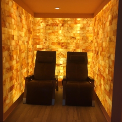 Two Brown Lounge Chairs In A Salt Room Surrounded By An Orange Backlit Salt Stone Wall At A Private Residence.