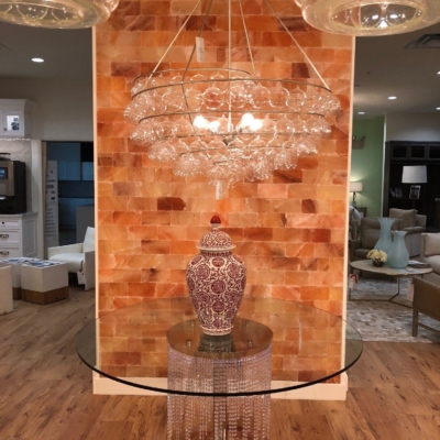 A Circular Glass Table In Front Of A Himalayan Salt Stone Wall With A Glass Chandelier Above At The Clive Daniel.