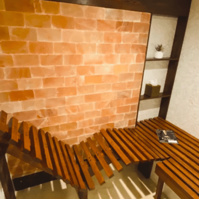 A Salt Stone Booth With A Wooden Seat In Front Of A Himalayan Salt Stone Wall And White Shiny Tiled Walls.