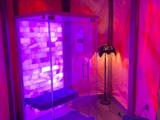 Glass Halotherapy Booth With A Salt Stone Wall Backlit With Purple Lighting In A Paneled Room Backlit With Purple And Orange Lighting At The Cryotherapy Plus Luxury Spa In Akron Ohio