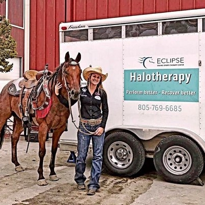 A Woman With A Cowboy Hat Holds The Reins Of A Horse As They Stand In Front Of A Trailer. The Trailer Has A Sign That Reads Eclipse Halotherapy, Perform Better, Recover Better And The Phone Number 805-769-6685