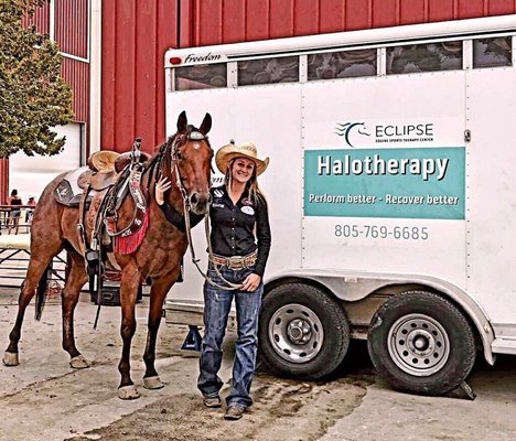 A Woman With A Cowboy Hat Holds The Reins Of A Horse As They Stand In Front Of A Trailer. The Trailer Has A Sign That Reads Eclipse Halotherapy, Perform Better, Recover Better And The Phone Number 805-769-6685