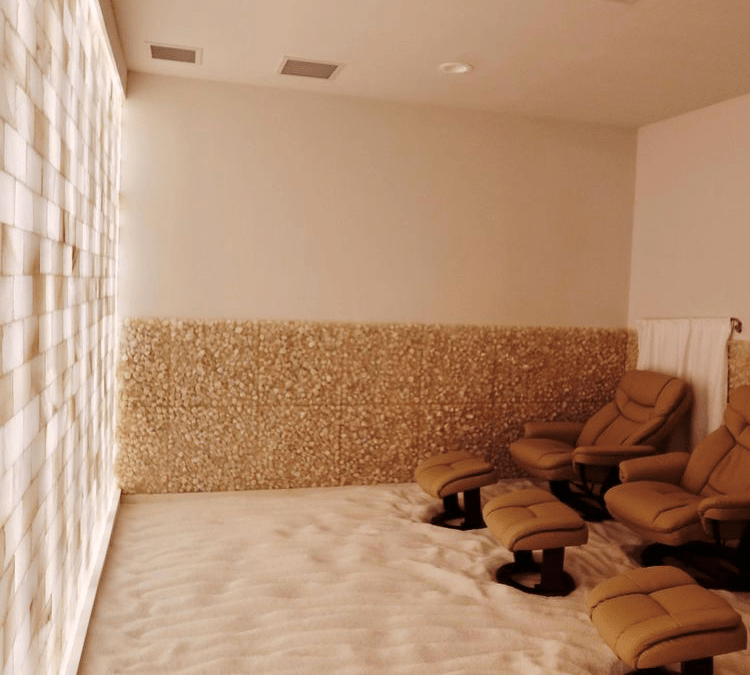 Two Light Brown Chair Both With A Light Brown Foot Rest On A Bed Of White Salt In A Room With A White Led Backlit Salt Brick Wall At Eleventh Element.