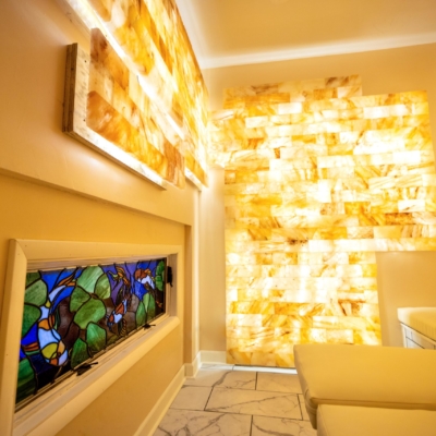 White Cushioned Booth With A Stained Glass Wall Piece And Led Backlit Salt Panels At Empowered Healing - Lincoln, Nebraska.