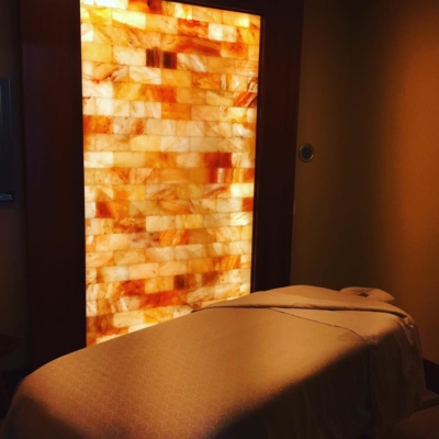 A Massage Table In Front Of A Orange Backlit Himalayan Salt Stone Wall At The Fahrenheit Body Spas.