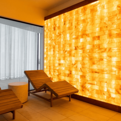 Two Wooden Chaises With A Circular Stone Stand Between With A Orange Backlit Salt Stone Wall With Orange Lighting.