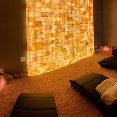 Four Black Chaises All With Pillows On A Himalayan Salt-Covered Floor Facing A Orange Backlit Salt Stone Wall At The Halo Salt Spa In Lincolnton, North Carolina