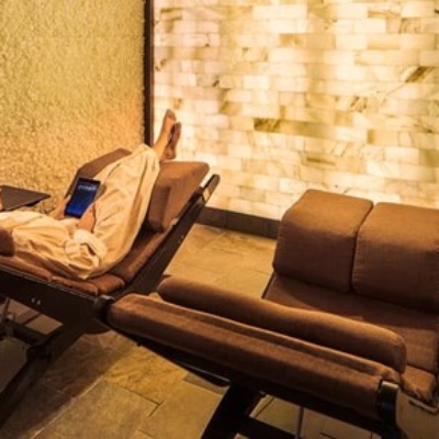 Woman relaxing on a lounge chair in a white robe with white salt bricks and a LED backlit salt panel wall surroundings a the Hyatt Regency Spa Avania - Scottsdale, Arizona.