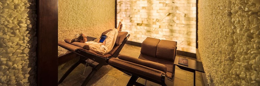 Two Brown Lounge Chairs Looking At A Led Back Lit Salt Brick Wall With A Lady In A White Robe Relaxing At The Hyatt Regency Spa Avania - Scottsdale, Arizona..