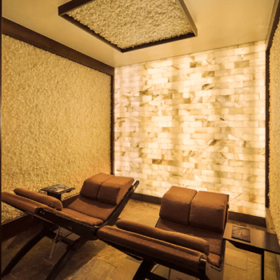 Two Brown Lounge Chairs In A Room Surrounded By White Salt Stone Walls And A White Back Lit Salt Stone Wall.