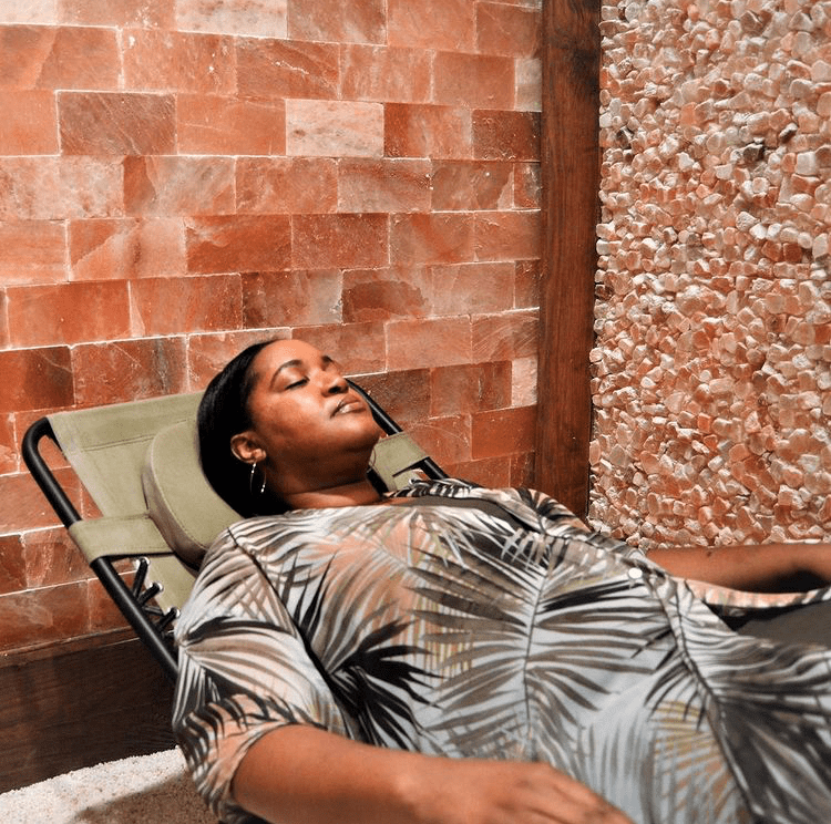 A Women Relaxed In A Reclining Lounge Chair With A Himalayan Salt Brick Wall And Panel At The Intown Salt Room.