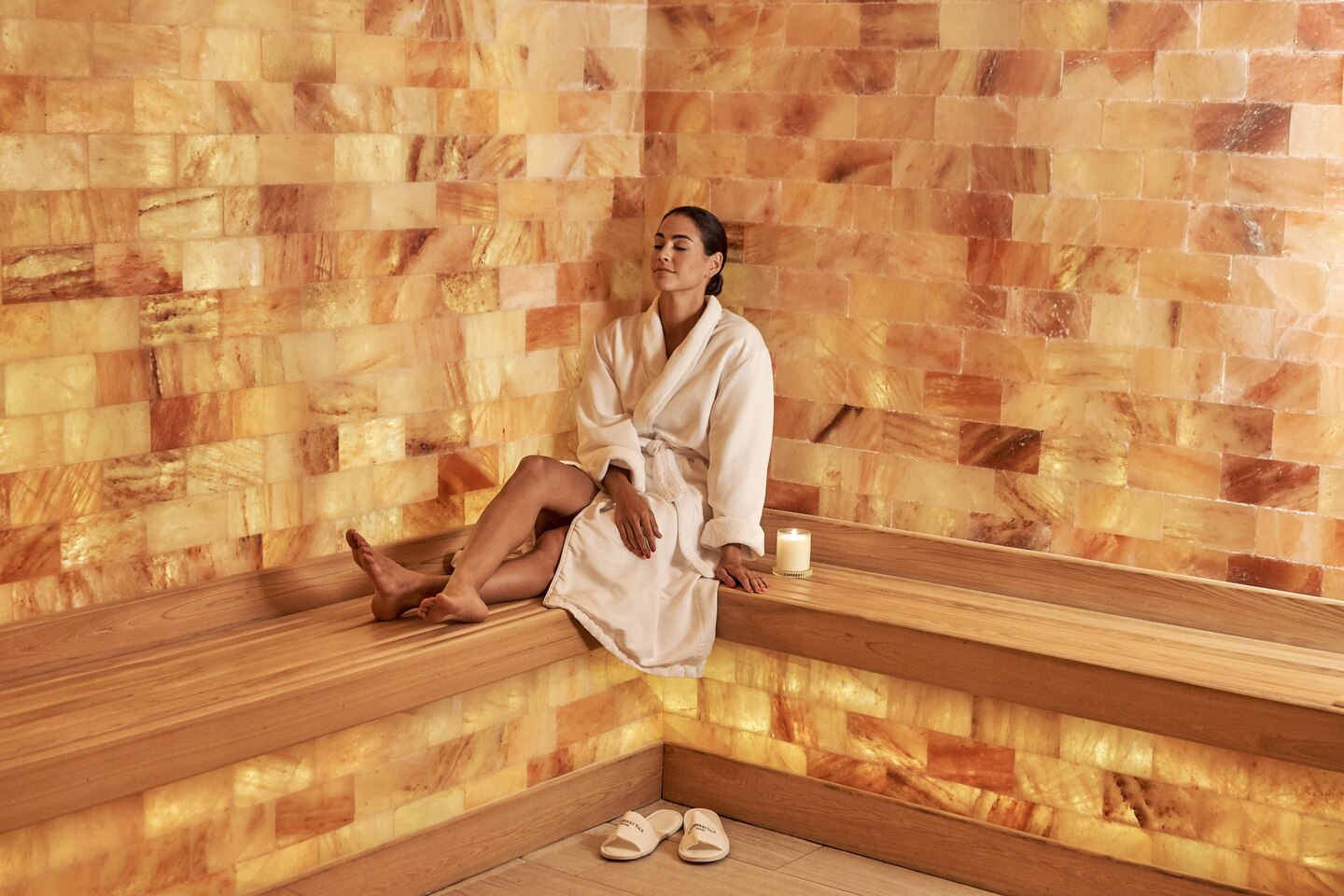 Woman In A White Robe Relaxing On A Light Brown Wooden Bench With Himalayan Salt Panel Walls At The Jw Marriott Turnberry - Aventura, Florida.