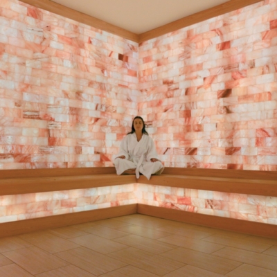 Women sitting crisscrossed in a white robe relaxing in front of an LED backlit Himalayan salt panel wall.
