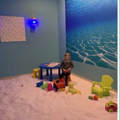 Young girl playing with toys on a salt-covered floor at a blue table in front of an ocean wallpaper at the Just Breathe Salt Spa in Hyannis, Massachusetts.