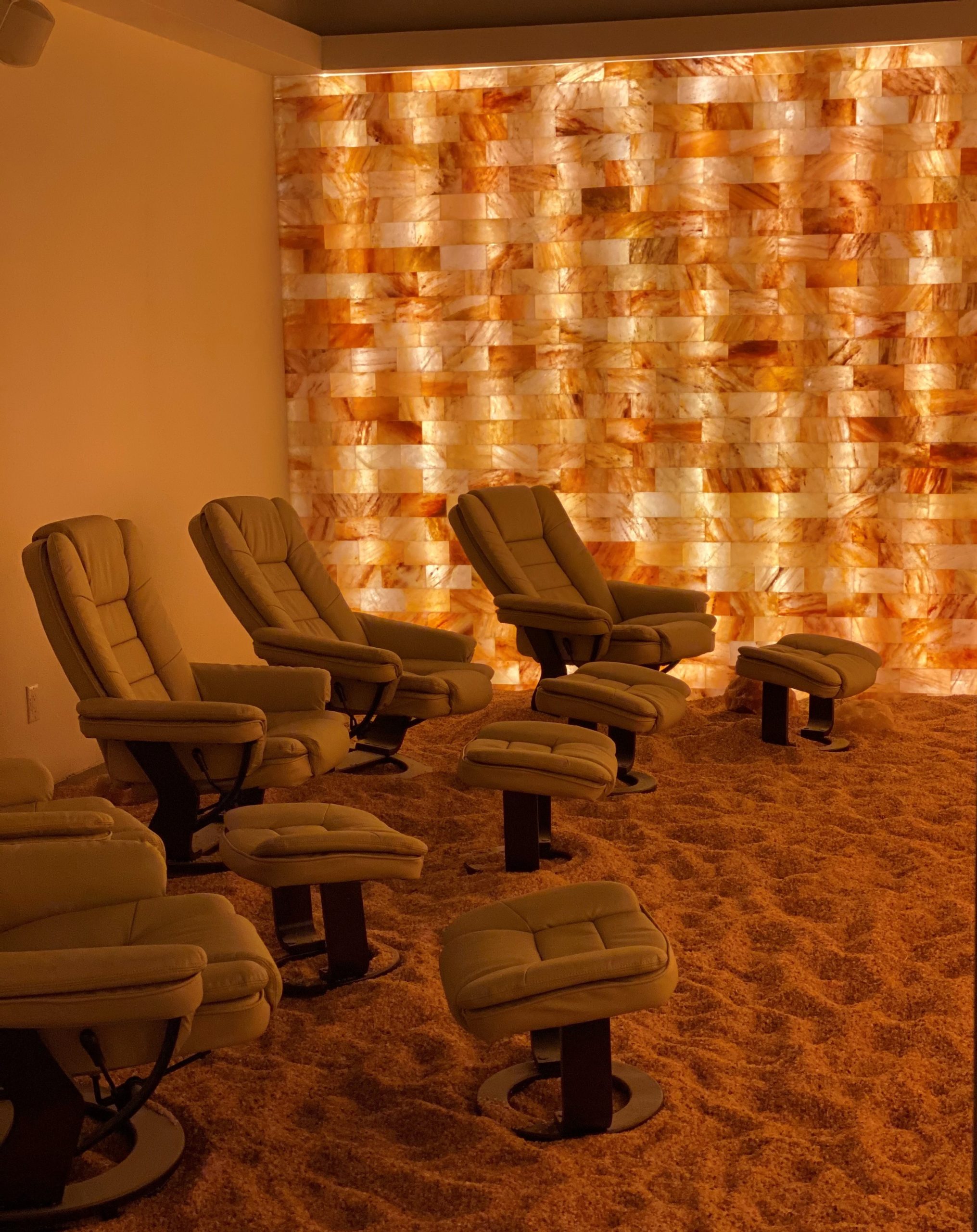 Five cushioned chairs on a Himalayan salt-covered floor next two a LED backlit salt panel wall.