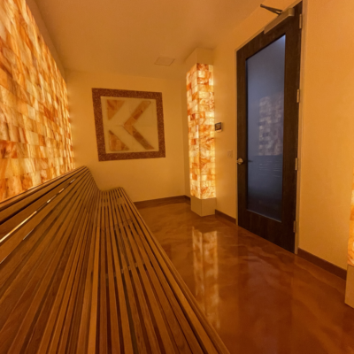 A Long Wooden Bench In A Room With A Glass Door With A Led Backlit Salt Brick Wall And Column And A Custom Salt Panel Of The Krysus Logo Design.