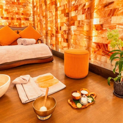 A large chaise with orange pillows and two rolled up towels surrounded by LED salt panel walls.