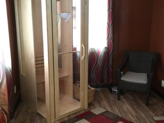 A Light Wooden And Glass Halotherapy Booth In A Red Room With Brown Vinyl Flooring And A Brown Chair In The Corner At The Lifetime Wellness Chiropractic Center