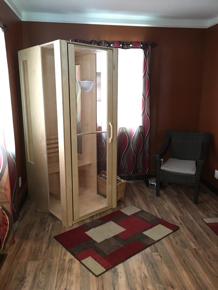 A light wooden and glass halotherapy booth in a red room with brown vinyl flooring and a brown chair in the corner at the Lifetime Wellness Chiropractic Center