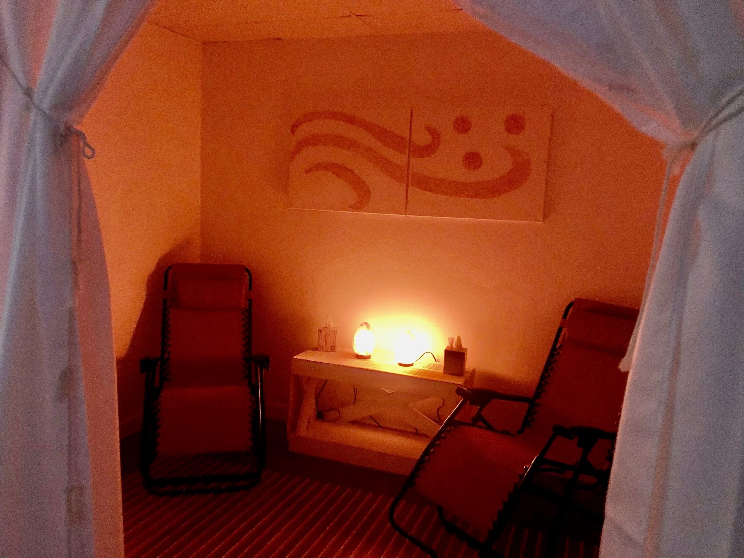 Two Red Lounge Chairs With A White Table Between With Two Himalayan Salt Lamps.