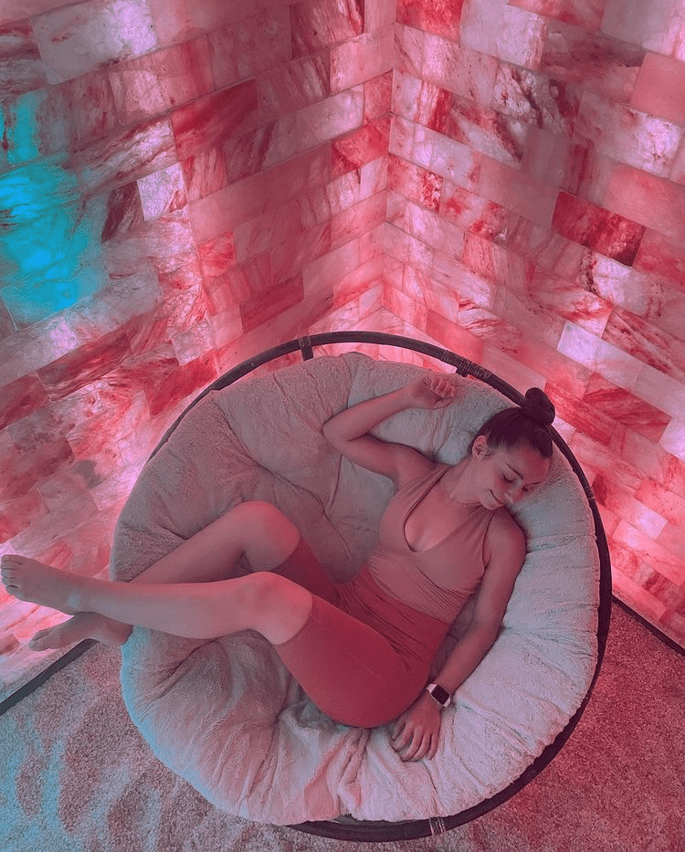 Woman Relaxing In A Circular Cushioned Chair On A Salt-Covered Floor Surrounded By Led Backlit Salt Panels At Modrn Sanctuary - New York City, Ny.