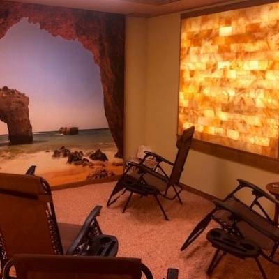 Four Reclining Chairs On A Salt-Covered Floor Facing An Ocean Wallpaper With A Square Salt Stone Panel Décor Backlit By Orange Lighting.