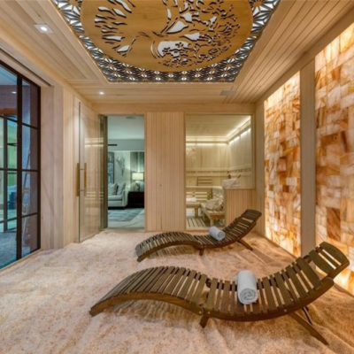 Two Wooden Chaises With Towels On Salt-Covered Floor Facing A Glass Door With A Himalayan Salt Stone Wall Behind.