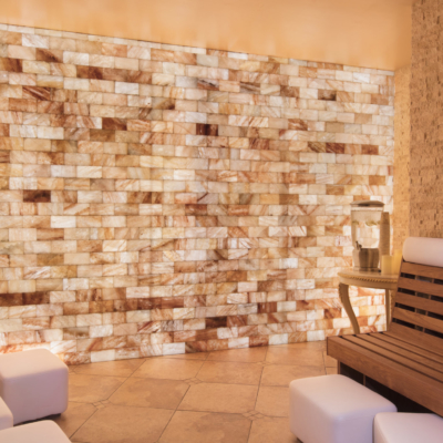 A Wooden Booth With Five White Foot Rests In A White Salt Tiled Room And An Orange Backlit Salt Stone Wall At The Peppermill Resort In Reno, Ca